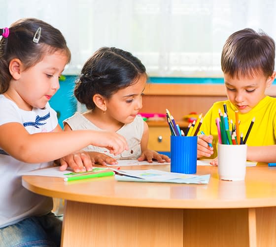 Tres niños en una mesa dibujando con lapices